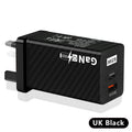 Compact black 65W GaN USB-C laptop charger with UK plug next to laptop