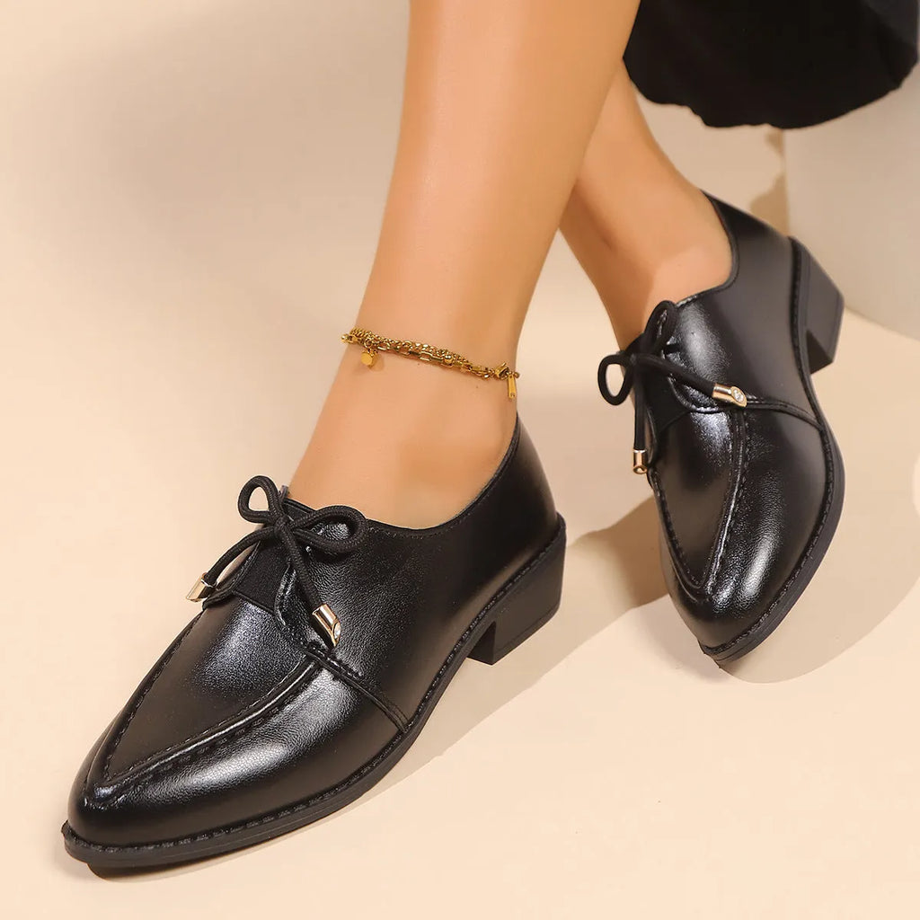 Women's brown slip-on flat shoes with a large bow decoration on the pointed toe.
