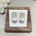 Silver tone dangle drop earrings with simulated pearl and sparkling clear stone on white background