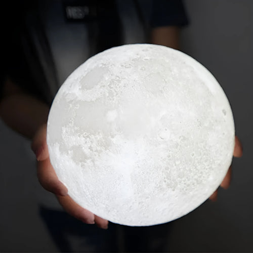 3D printed white moon lamp on a wooden stand, showing detailed lunar surface texture.