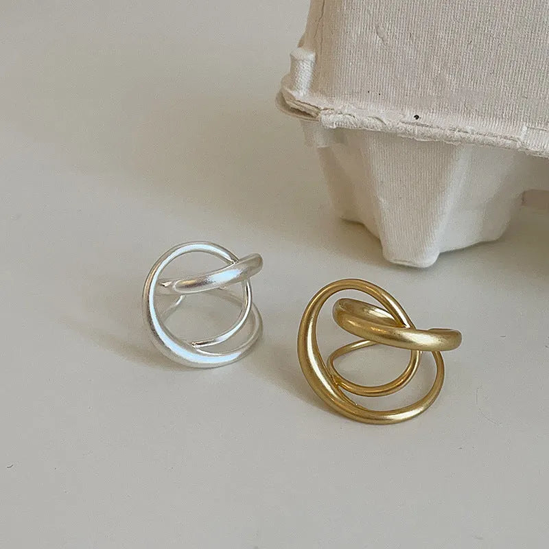 Geometric open ring with 3D interlaced matte metal design in gold or silver finish.