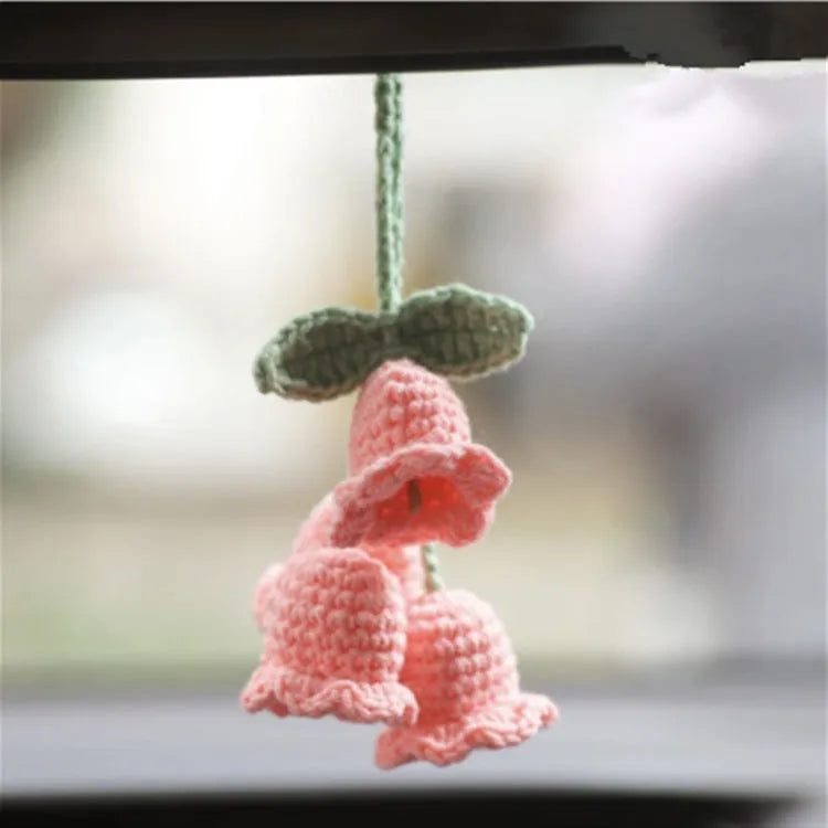 Green and white knitted wool car plant decoration with hanging rope on a car dashboard.