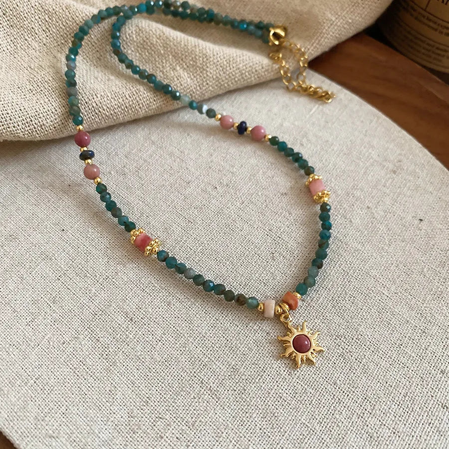 Freshwater pearl necklace with blue stone sun pendant on a gold-tone adjustable chain.