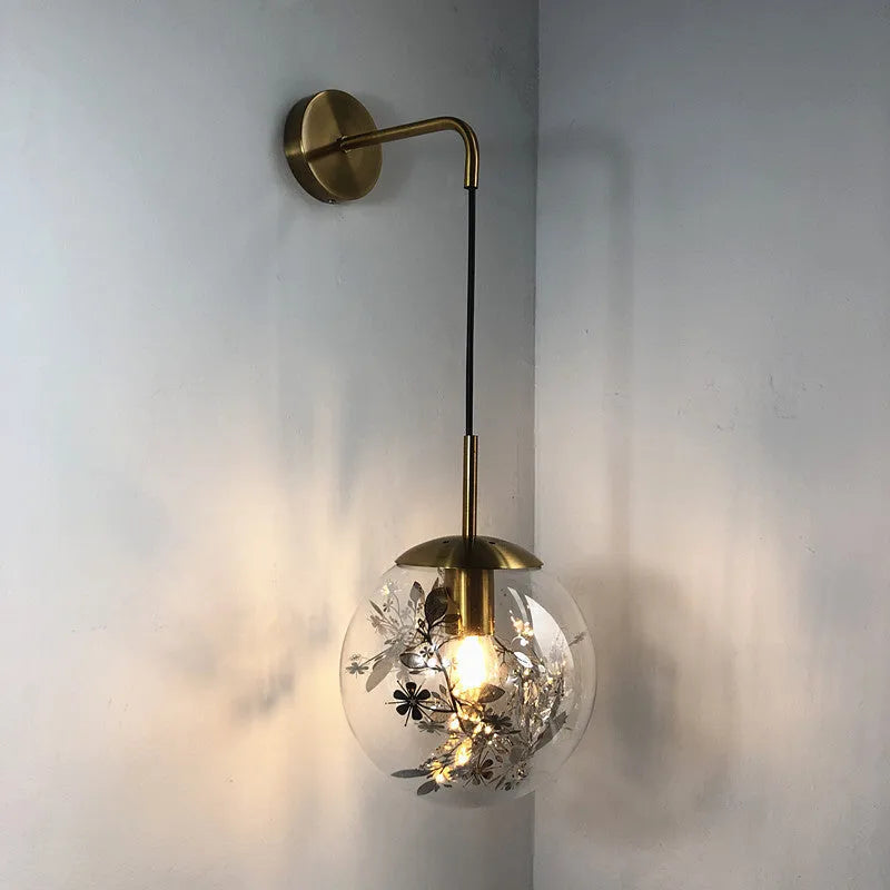 Simple modern glass wall lamp in golden flower finish mounted beside a bed.