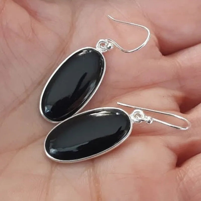 Oval black agate stone set in a geometric silver electroplated frame, forming a drop pendant earring for women.
