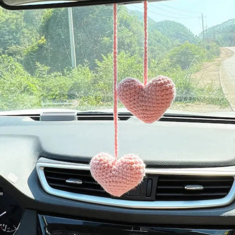 Green and white knitted wool car plant decoration with hanging rope on a car dashboard.