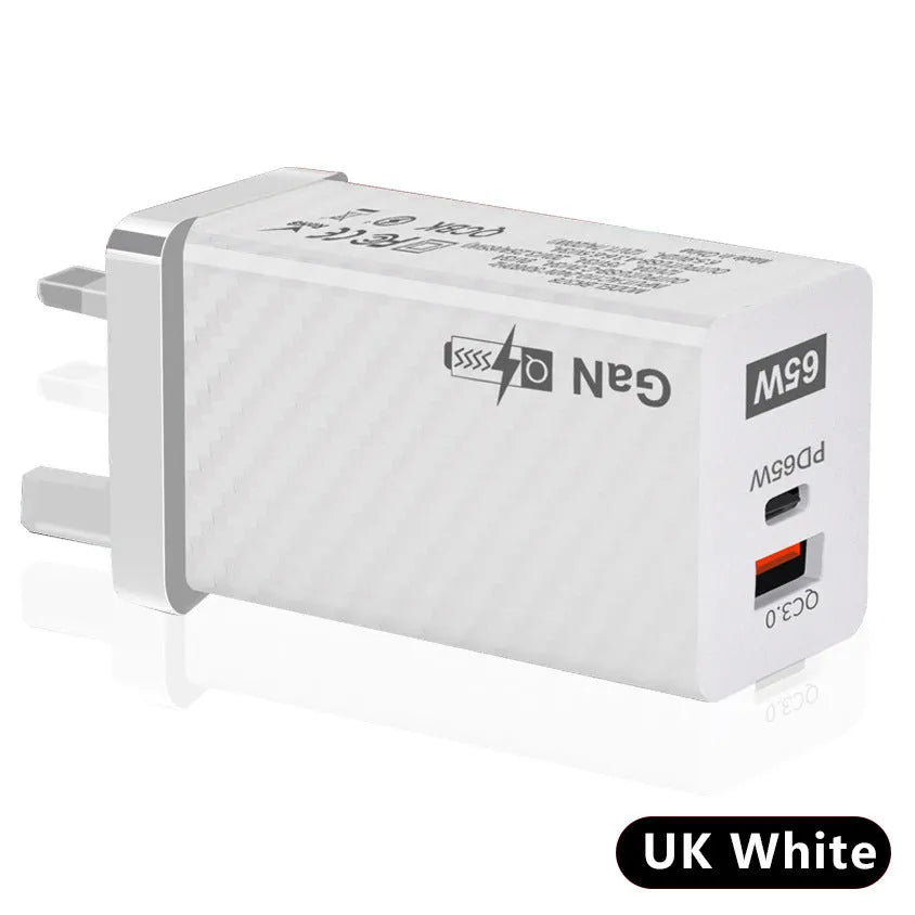 Compact black 65W GaN USB-C laptop charger with UK plug next to laptop
