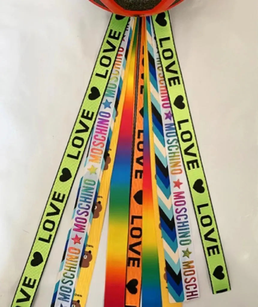 Colourful fabric helmet streamers for children's roller skating and ski helmets, shown in apricot, red, and grey.