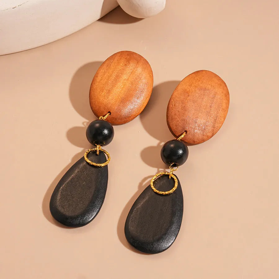 Close-up of handmade wooden elliptical earrings in silver, brown, and black colours on a retro-style background.