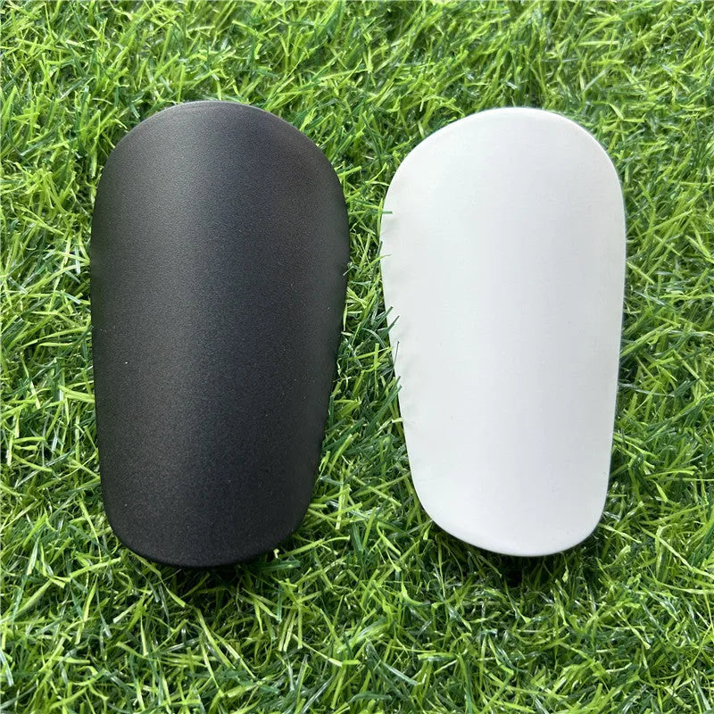 Extra small black and white plastic football shin guards for junior players, shown at 8x5 cm size.