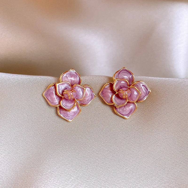 Close-up of a pair of purple and gold flower stud earrings with a textured oil-spot glaze finish.