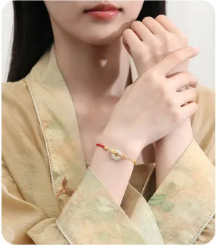 Women's silver bracelet with gold peace buckle and koi fish charm on a red rope.
