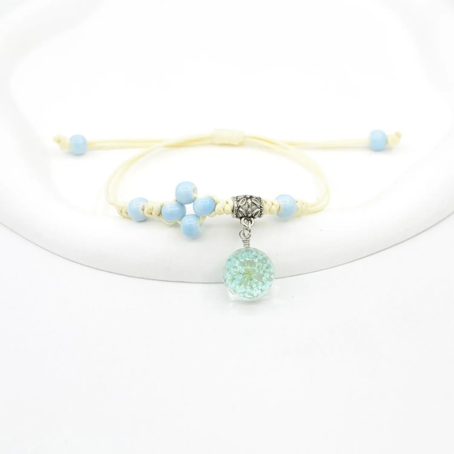 Close-up of a hand-woven glass bracelet with large beads containing real dried flowers and a lace design.
