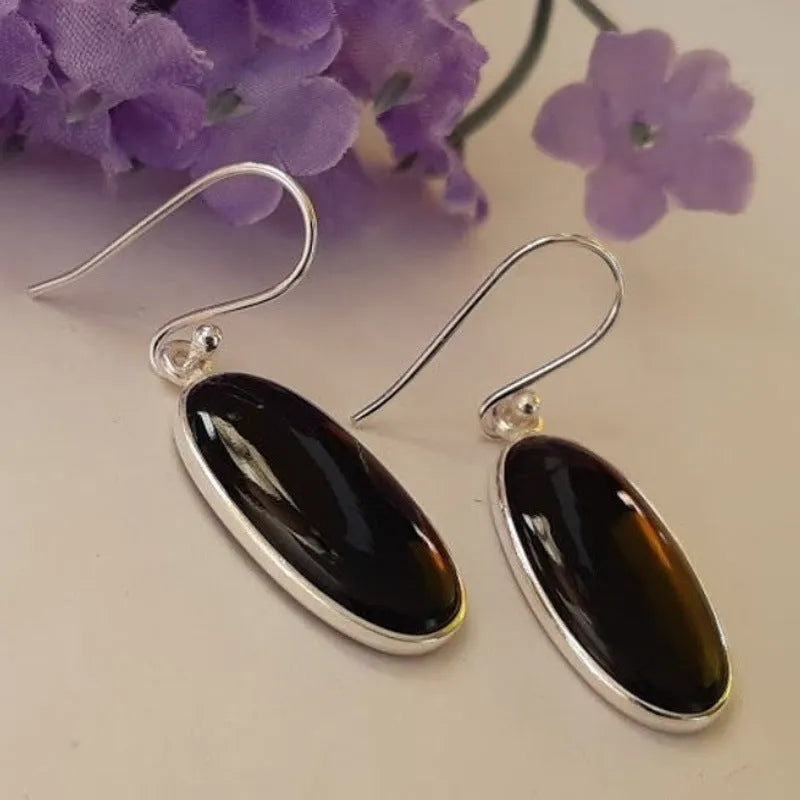 Oval black agate stone set in a geometric silver electroplated frame, forming a drop pendant earring for women.