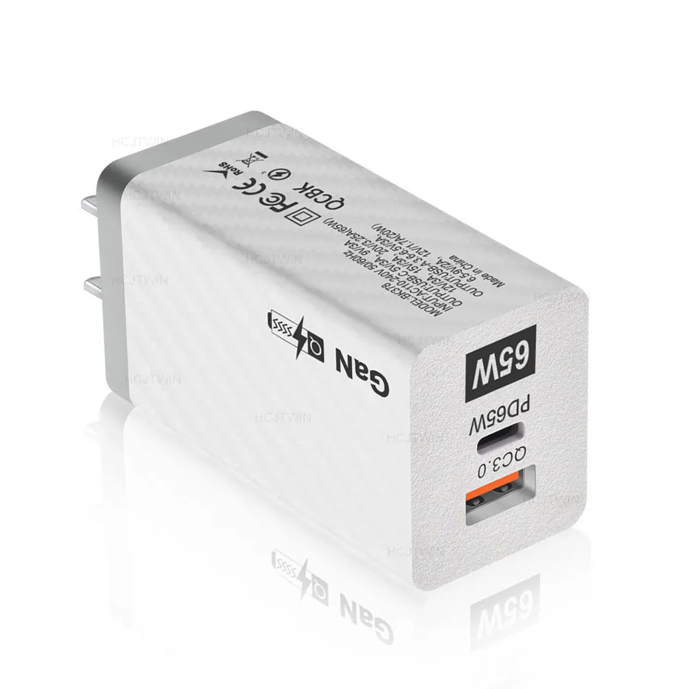 Compact black 65W GaN USB-C laptop charger with UK plug next to laptop