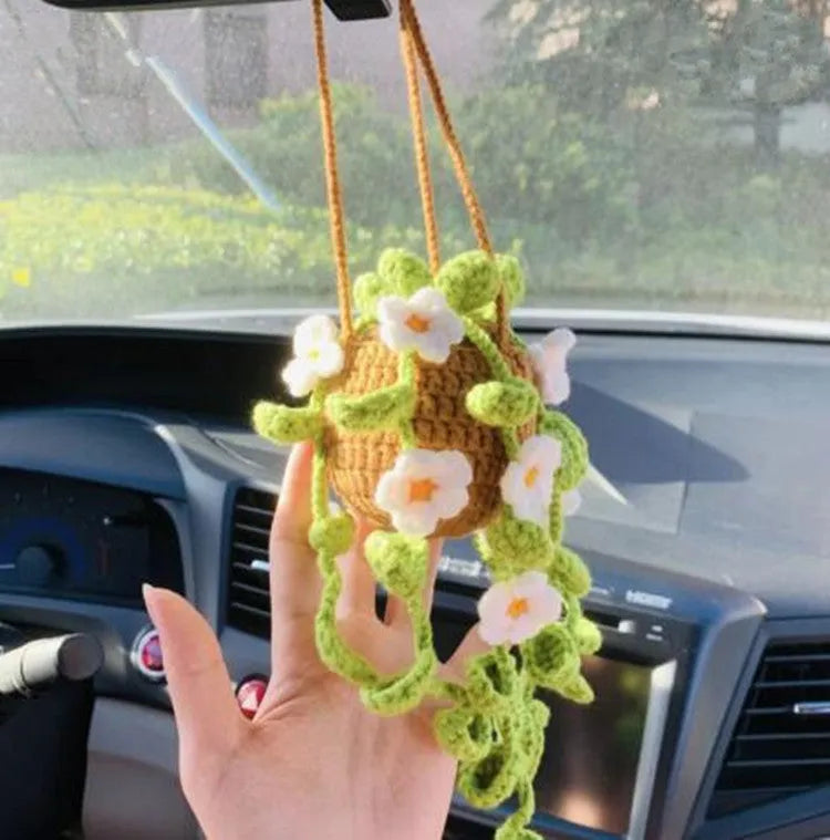 Green and white knitted wool car plant decoration with hanging rope on a car dashboard.