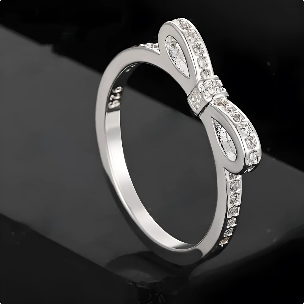 Silver bow-shaped ring with rhinestone and zircon crystal details on a model finger.