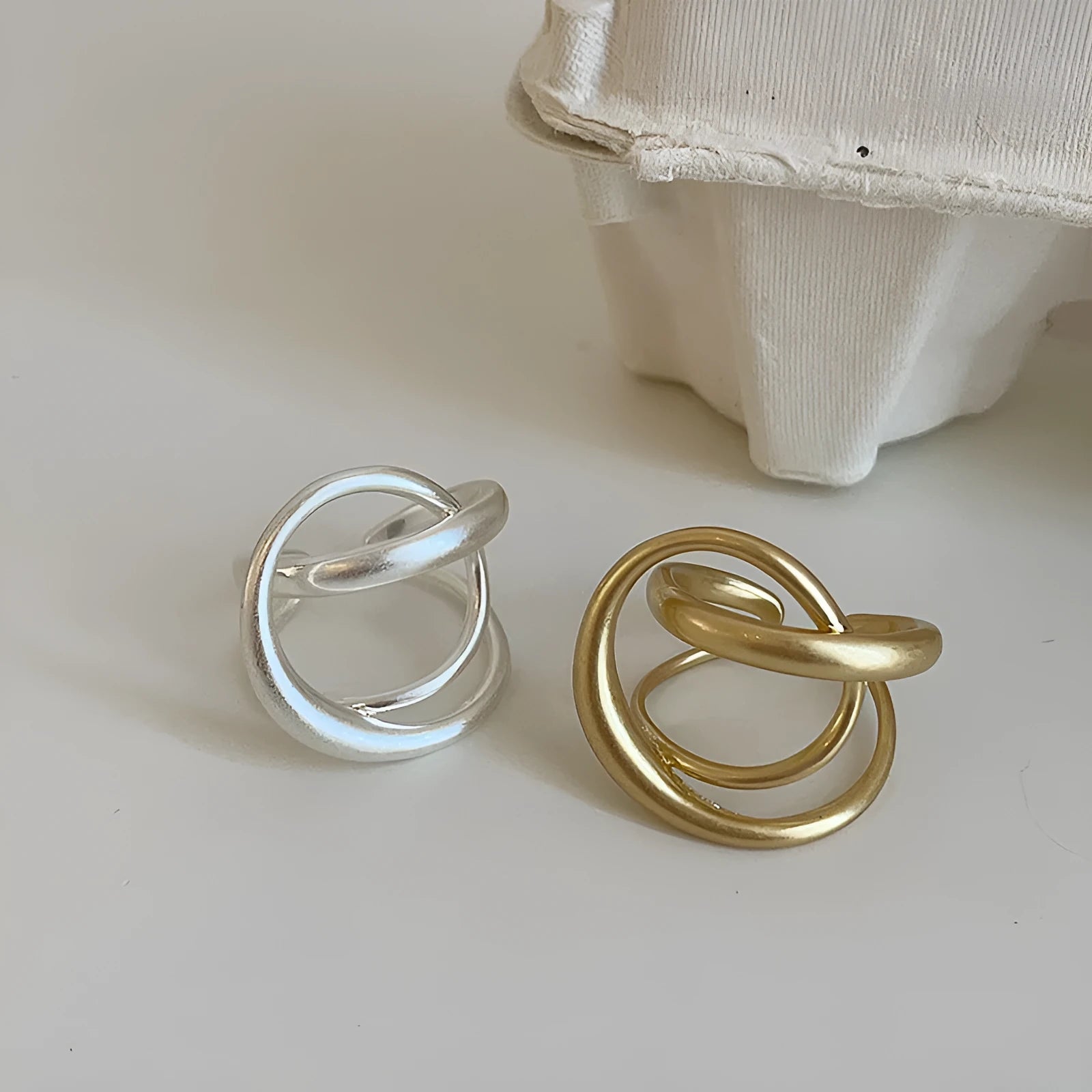 Geometric open ring with 3D interlaced matte metal design in gold or silver finish.