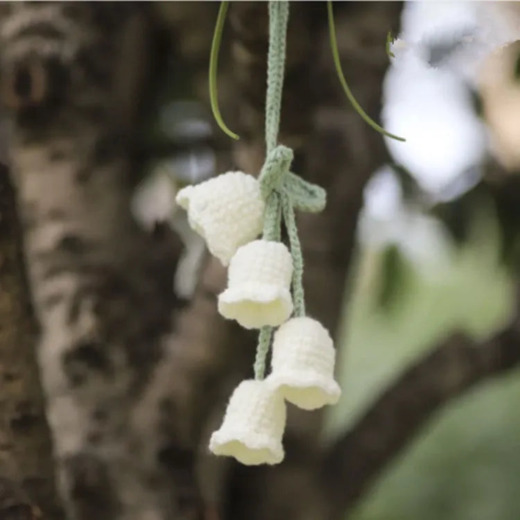 Green and white knitted wool car plant decoration with hanging rope on a car dashboard.