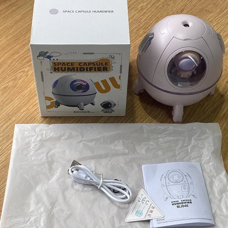 Purple astronaut-themed desktop USB humidifier with LED light next to USB cable on a desk.