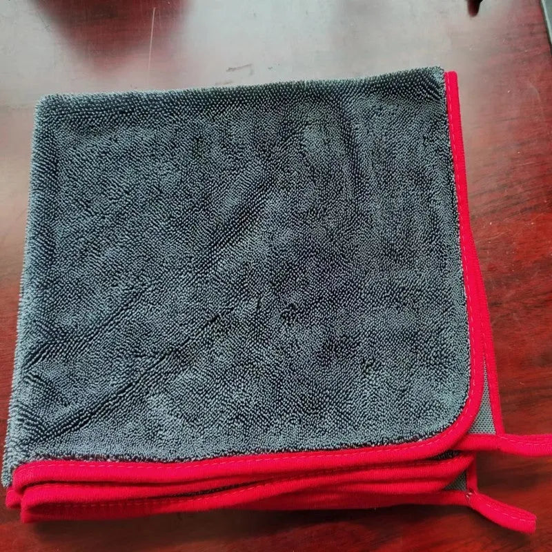 Grey braided car cleaning towel with red edge trim shown drying a car windscreen.