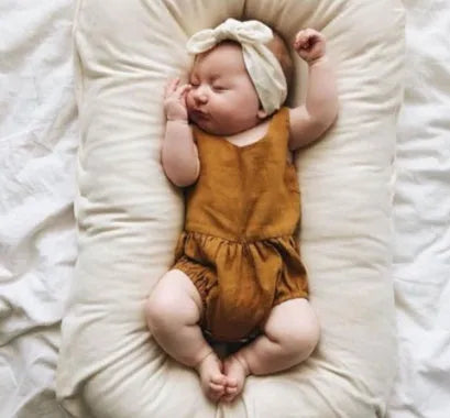 Beige portable baby nest crib for newborns measuring 75cm by 45cm on a neutral background.