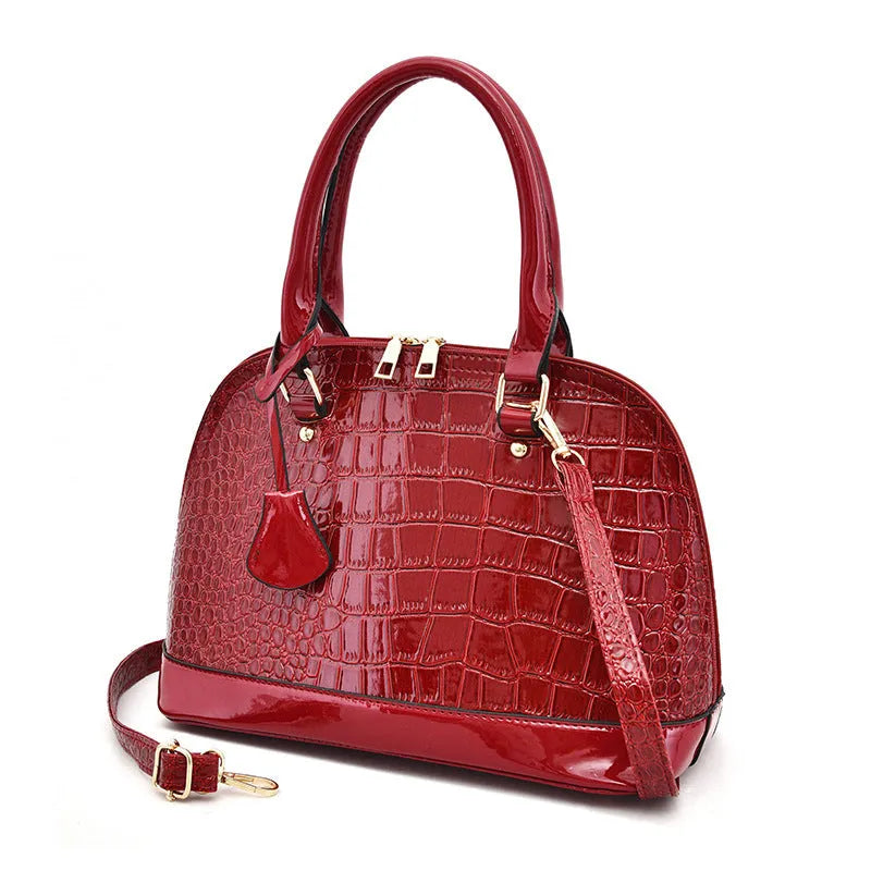 Large shiny black crossbody shoulder bag with a structured shell shape.