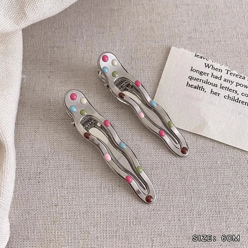Two shiny silver metal duckbill barrettes with hollow star patterns on a plain background