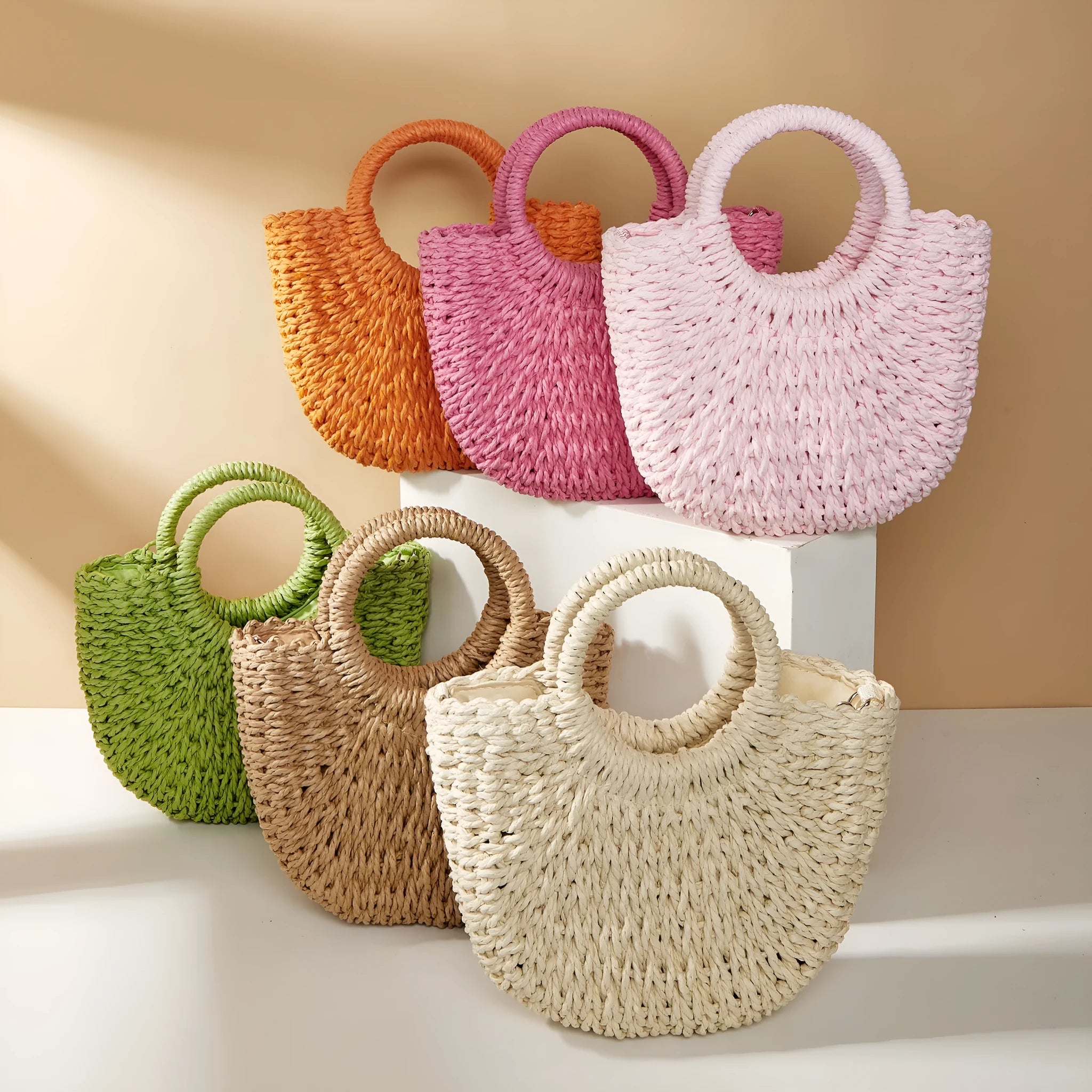 Woven straw beach bag in beige, peach skin lining, crossbody style, 24cm height, on a sandy beach