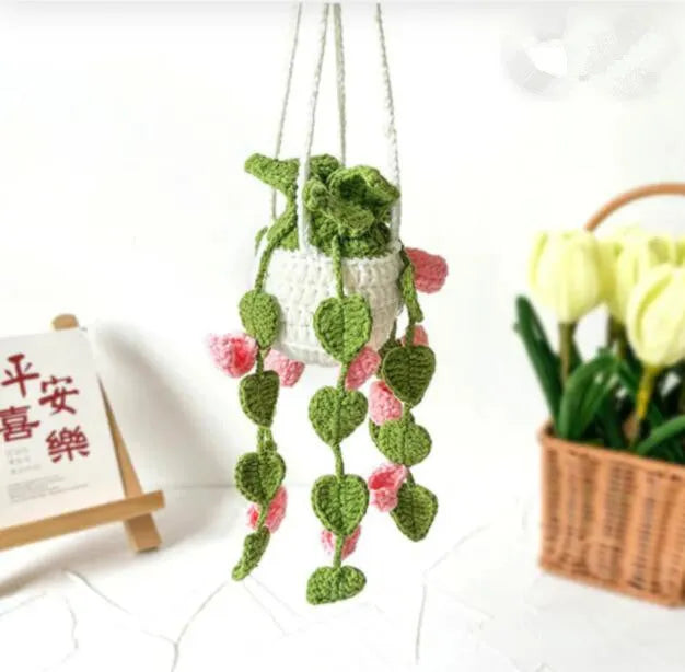 Green and white knitted wool car plant decoration with hanging rope on a car dashboard.
