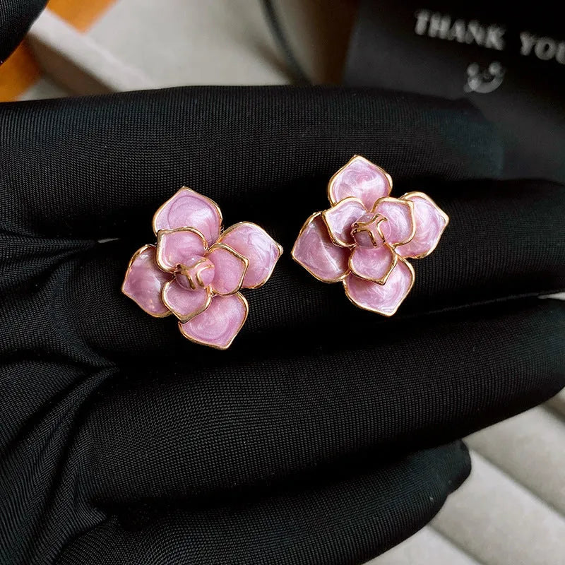 Close-up of a pair of purple and gold flower stud earrings with a textured oil-spot glaze finish.
