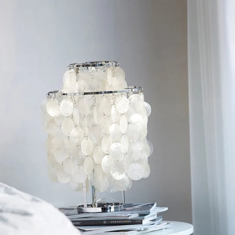 Modern bedside table lamp with a decorative white shell-shaped shade on a metallic chrome or gold base.