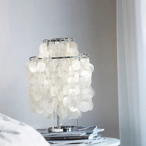 Modern bedside table lamp with a decorative white shell-shaped shade on a metallic chrome or gold base.