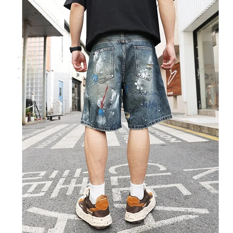 Blue men's ripped denim shorts with graffiti detailing and a straight-leg cut, showing front zipper fly.
