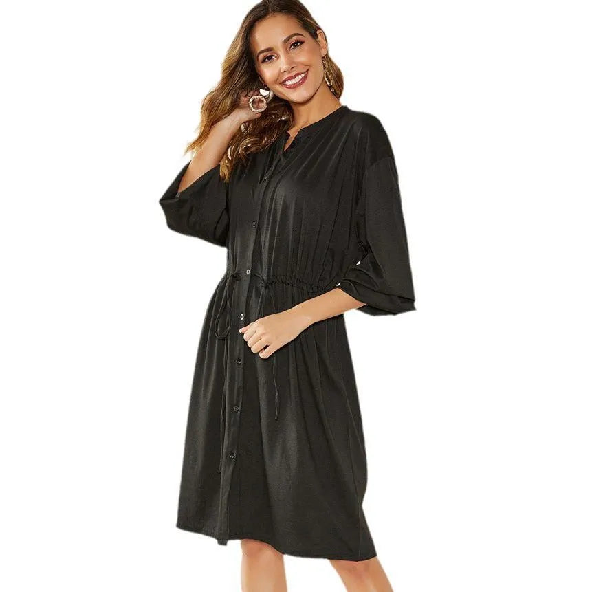 A black A-line midi dress with long sleeves, elasticated cuffs and waist, shown with a belt.