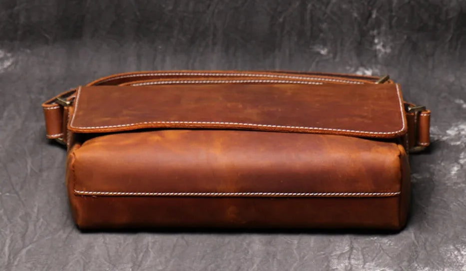 Men's vintage brown cowhide medium messenger bag showing front flap and long shoulder strap.
