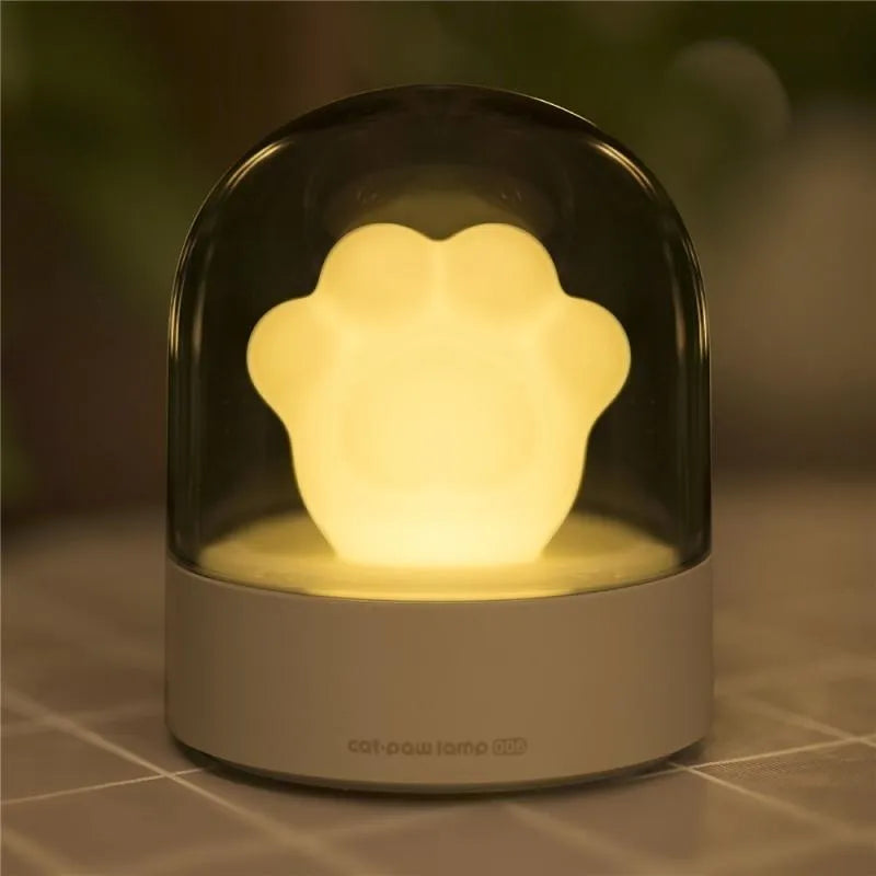 Grey cat paw shaped USB rechargeable night light and music box lamp on a desktop.