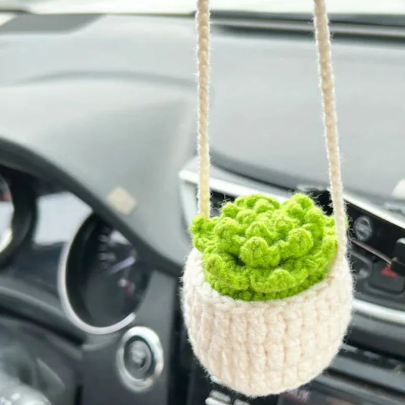 Green and white knitted wool car plant decoration with hanging rope on a car dashboard.