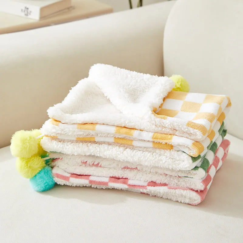 Green plaid pet fleece blanket with fur ball decoration on a sofa for a cat or dog.