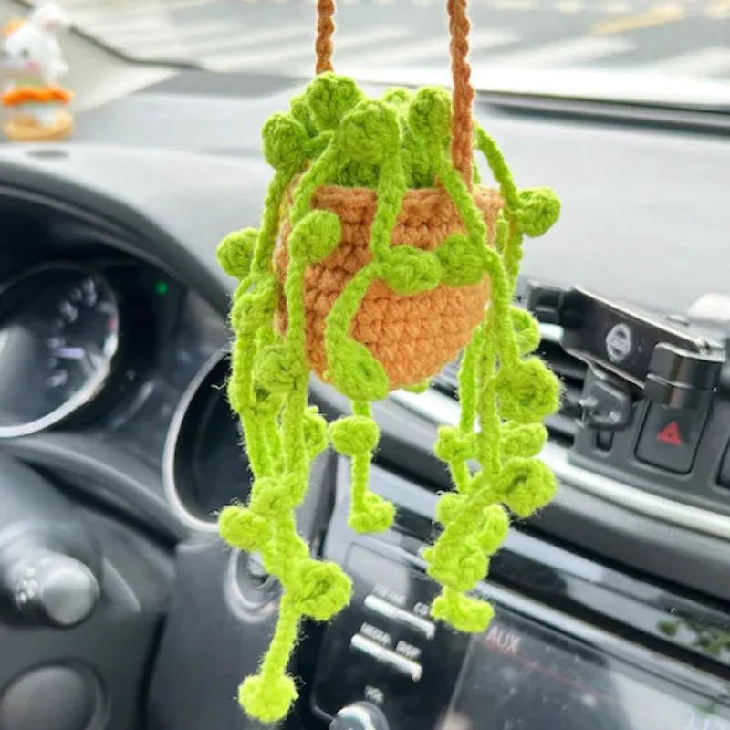 Green and white knitted wool car plant decoration with hanging rope on a car dashboard.