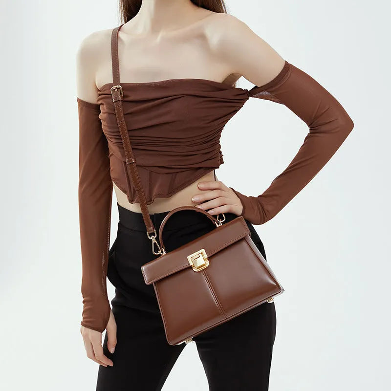 Women's black leather shoulder bag with vachette clasp, showing horizontal square shape and adjustable strap