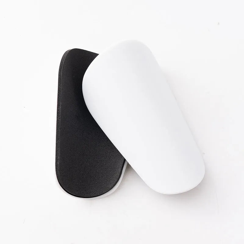 Two pairs of PU mini shin guards in black, white, red, and dream blue colours on a sports field.