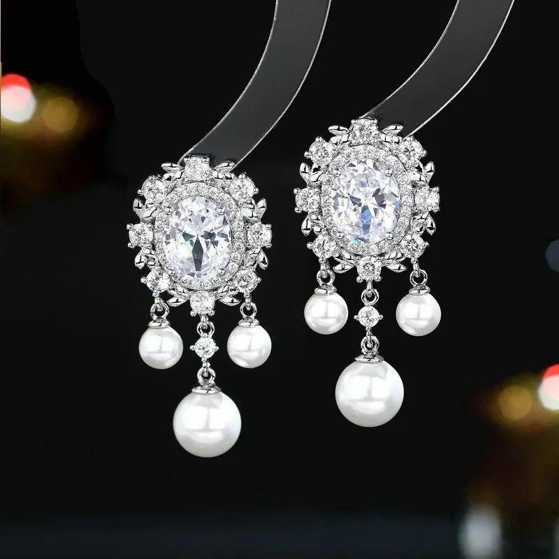 A pair of oval-shaped copper earrings with zircon inlay and a light-coloured pearl tassel.