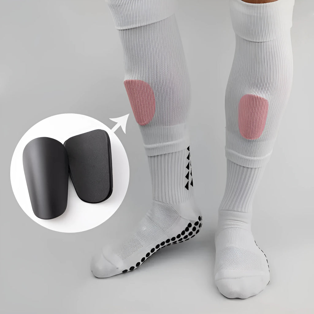 Two pairs of PU mini shin guards in black, white, red, and dream blue colours on a sports field.