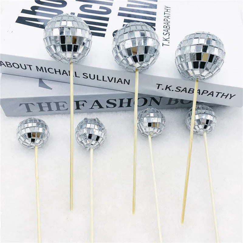 Glass disco ball cake decoration with wooden stick in various sizes on a birthday cake.