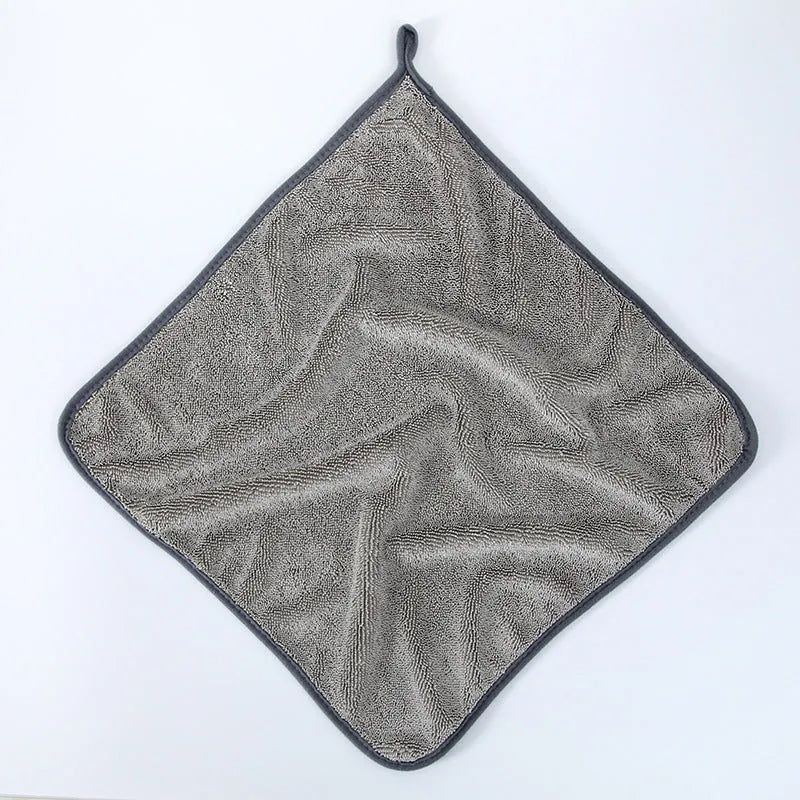 Grey braided car cleaning towel with red edge trim shown drying a car windscreen.