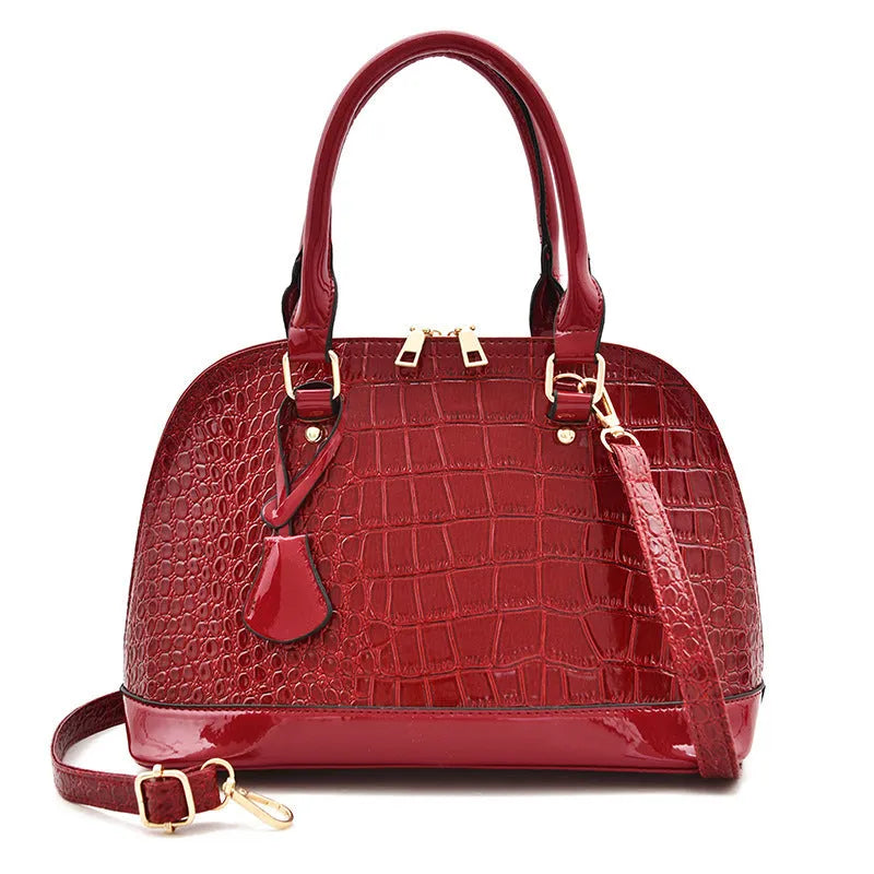 Large shiny black crossbody shoulder bag with a structured shell shape.