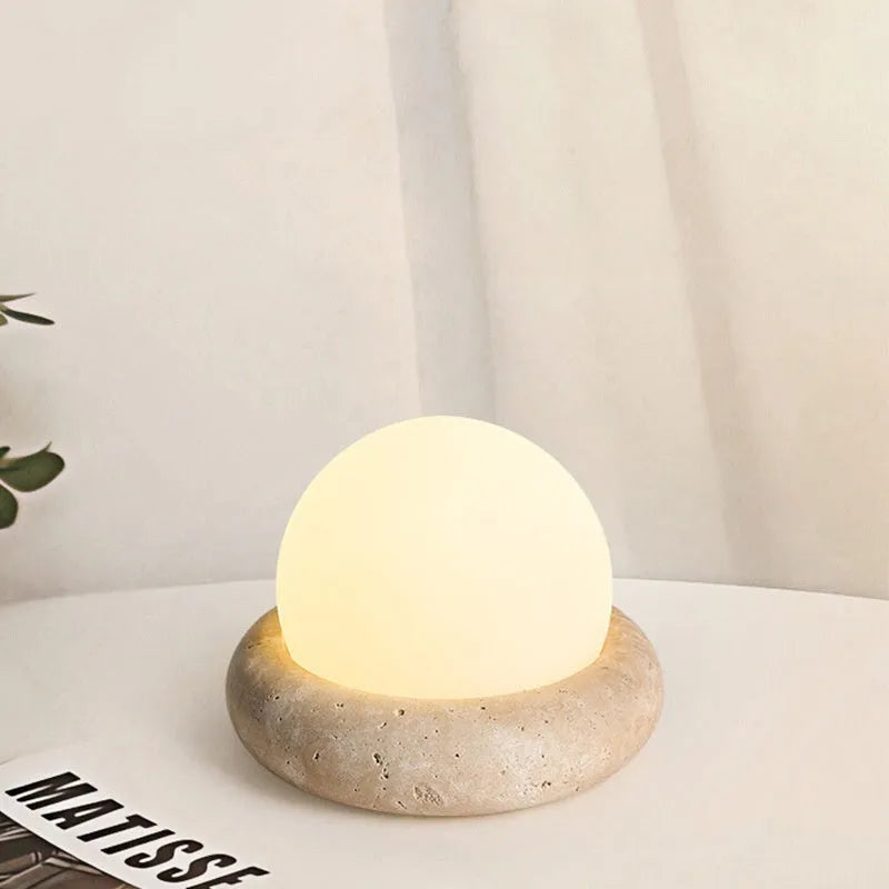 Cream coloured round rechargeable remote control night light on a bedside table.