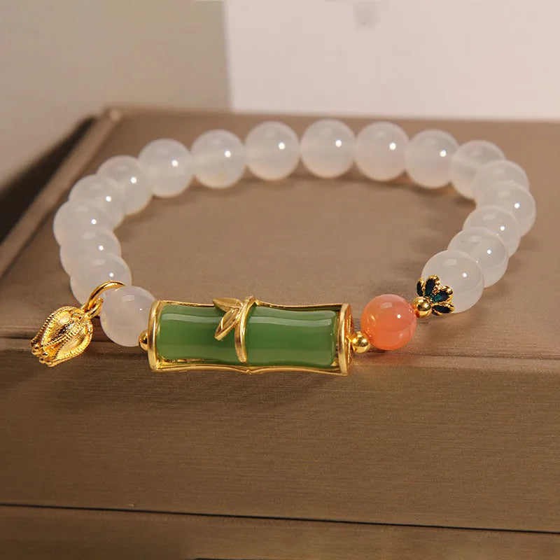 Close-up of a women's bracelet with a white agate jade bead and bamboo joint design on a natural background.