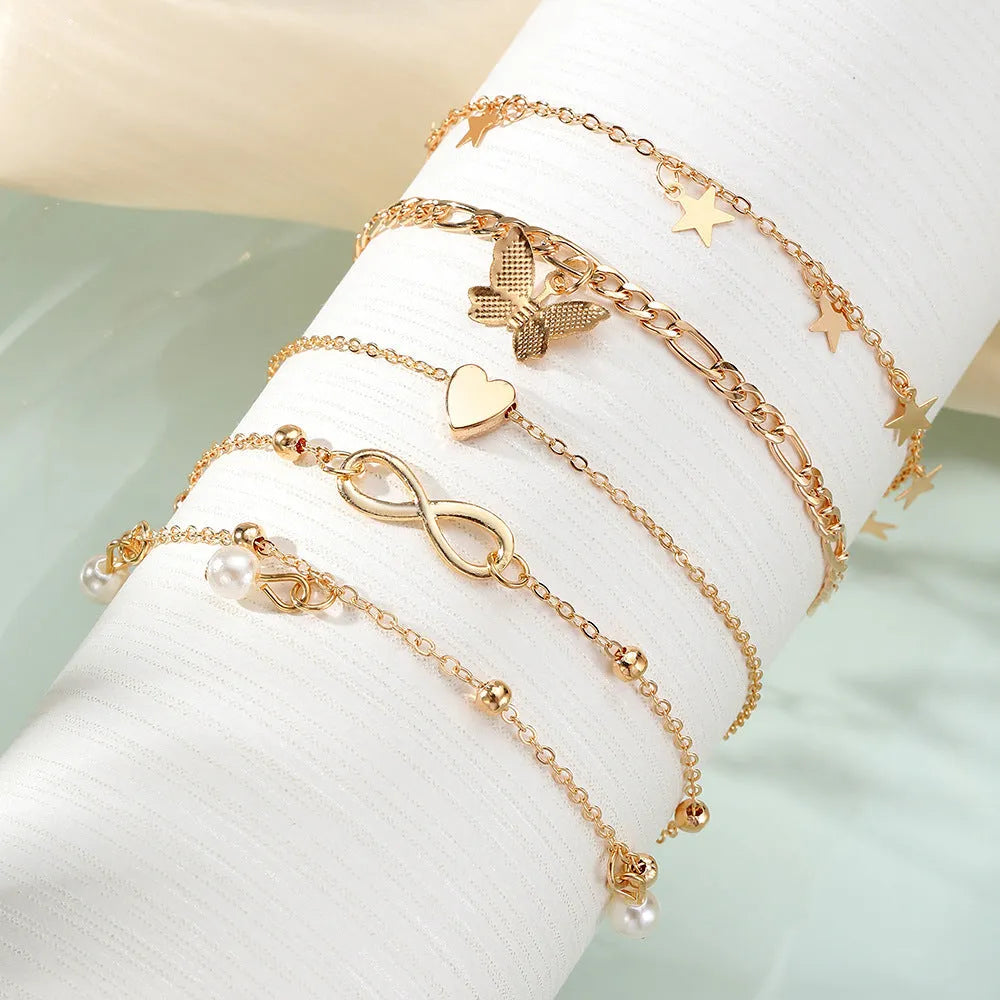 Four gold-tone alloy anklets with butterfly and heart pearl charms arranged as a set
